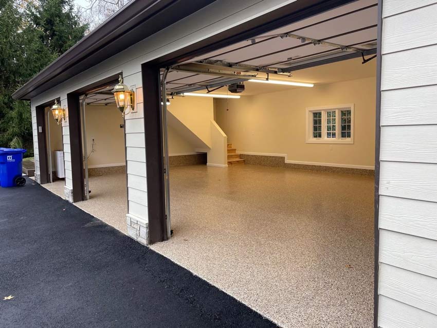 Spacious, clean, three-car garage with open doors, speckled epoxy floor
