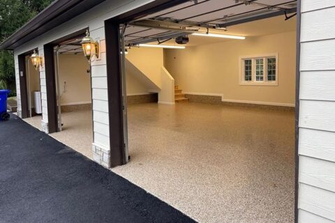 Spacious, clean, three-car garage with open doors, speckled epoxy floor